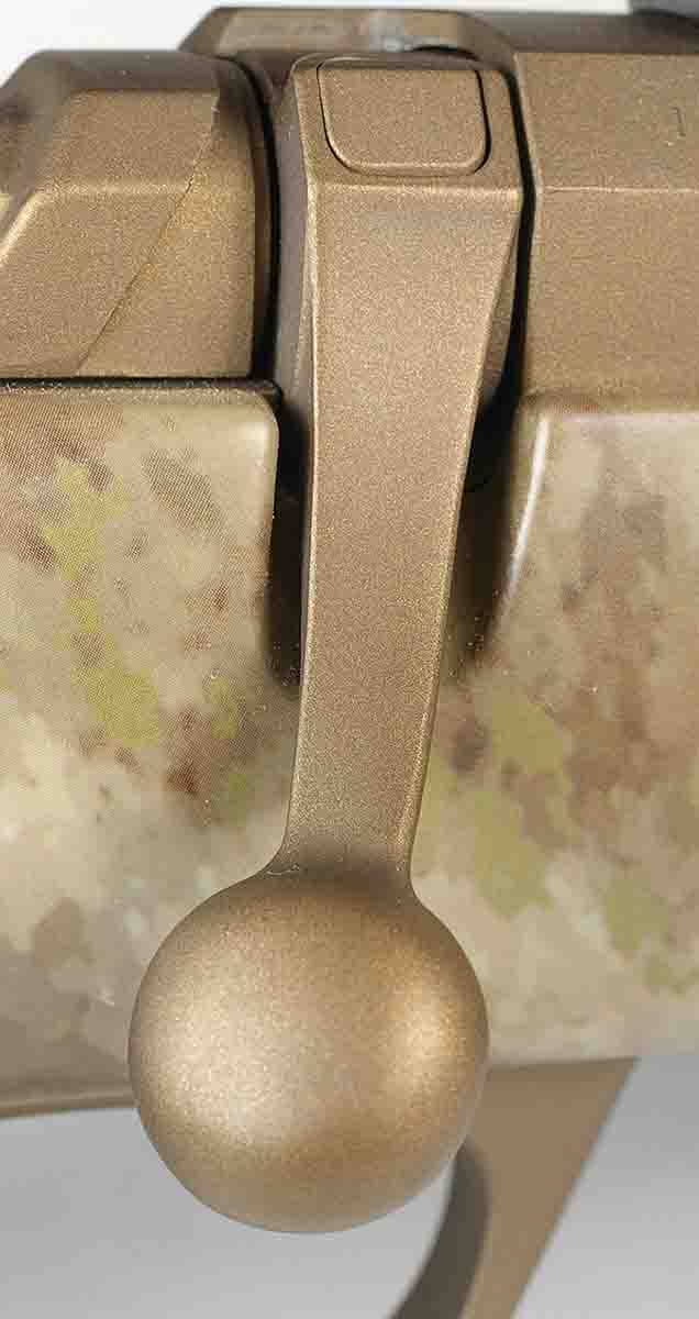 A push-button lock at the top of the bolt handle keeps it shut. Pushing the lock allows opening the bolt with the safety engaged.